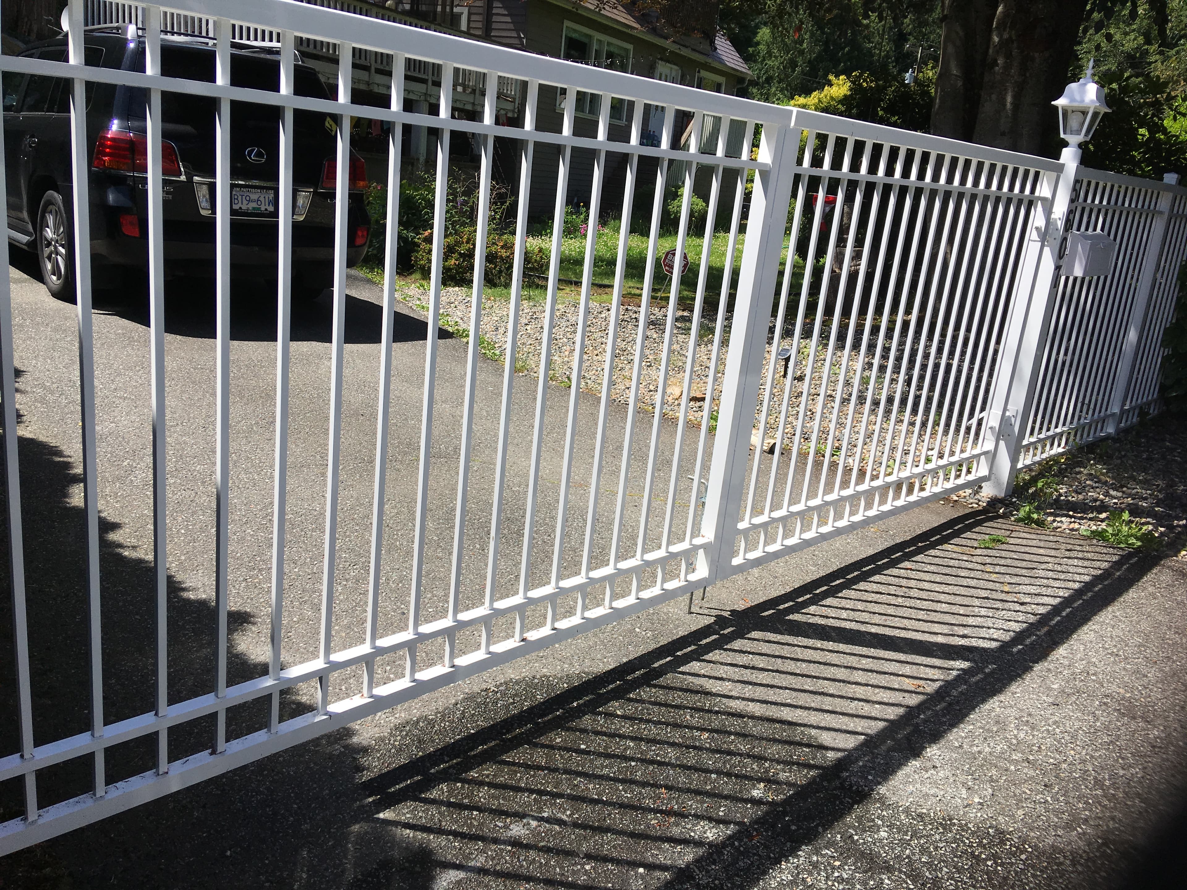 White sliding driveway gate with matching picket fence